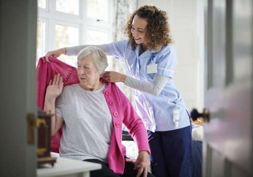 home carer helping senior woman get dressed in her bedroom