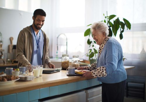 A young caregiver serving breakfast to elderly woman in nursing home care center.