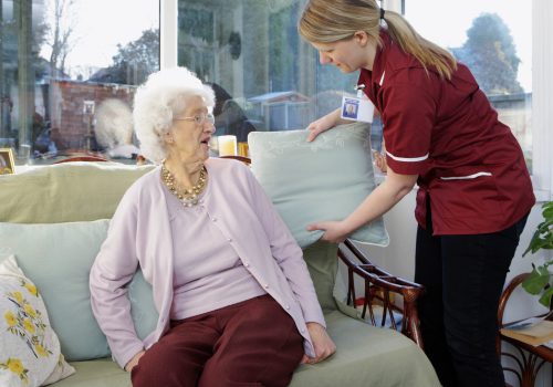 carer fluffs up her elderly pactient cushions to make her more comfortable
