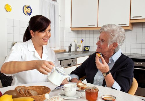 a geriatric nurse helps elderly woman at breakfast